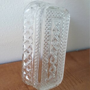 May include: A clear glass butter dish with a diamond pattern. The dish is rectangular and has a lid.