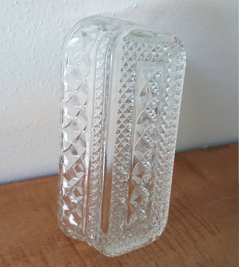 May include: A clear glass butter dish with a diamond pattern. The dish is rectangular and has a lid.