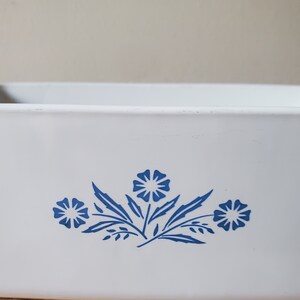 Puede incluir: Plato para hornear de cer&aacute;mica blanca con un dise&ntilde;o floral azul. El dise&ntilde;o presenta tres flores estilizadas con hojas.
