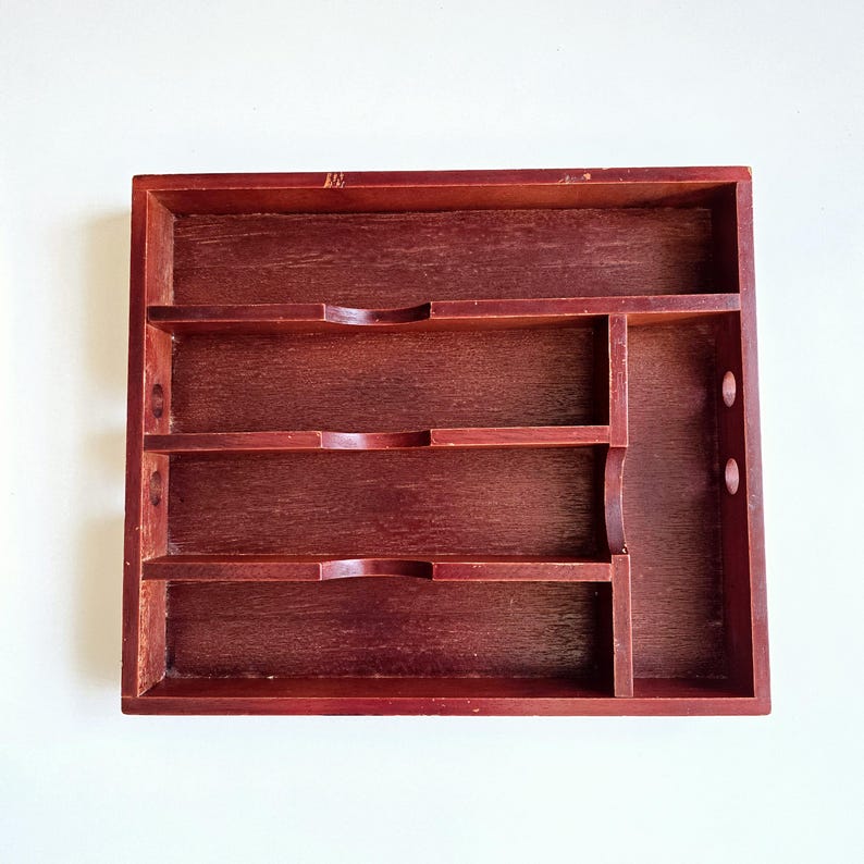 May include: A dark red wooden organiser with multiple compartments. It features three shelves with curved cutouts and a vertical section with two circular holes. The wood grain is visible throughout the piece.