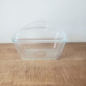 May include: A clear glass rectangular baking dish with a lid and a handle. The dish has a textured bottom.