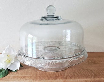 May include: A clear glass cake stand with a domed lid. The stand has a decorative, swirling pattern and the lid has a knob on top.