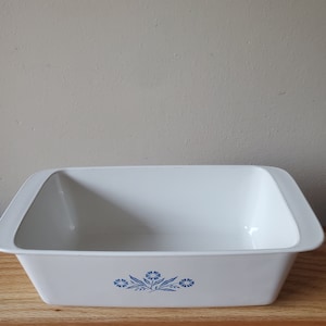 Puede incluir: Plato para hornear de cer&aacute;mica blanca con un dise&ntilde;o floral azul. El plato es rectangular y tiene un borde ligeramente elevado.