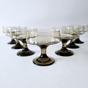 May include: Set of six clear glass stemmed dessert dishes with a brown tinted base. The dishes are arranged in a row on a white surface.