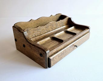 May include: A wooden desk organizer with a warm brown finish. It features a wavy top section, three small square compartments, and a small drawer with a metal knob. The organizer is designed to hold various office supplies.