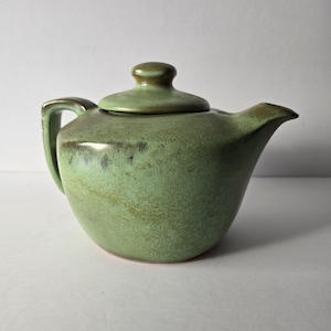 May include: A green ceramic teapot with a lid. The teapot has a mottled glaze with brown and green accents.