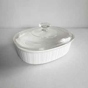 May include: White oval casserole dish with a clear glass lid. The dish has vertical ribbed detailing on the sides. The lid has a clear knob handle. This dish is suitable for baking and serving.