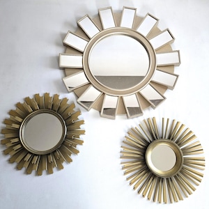May include: Three circular wall mirrors with sunburst designs. The largest mirror features wide, rectangular mirrored rays. The two smaller mirrors have thin, pointed metallic gold rays surrounding a central circular glass reflective surface.