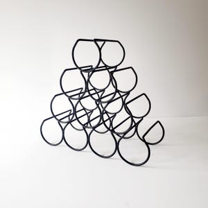 May include: A matte black metal wine rack featuring a pyramid-shaped structure with ten circular bottle holders arranged in four tiers. The frame is constructed from thin, curved wire rods that create a geometric, open design for storage.