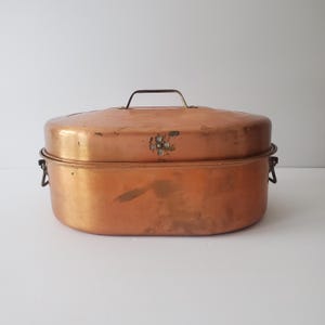 May include: A vintage copper roasting pan with a lid and two handles. The pan has a decorative floral design on the lid.
