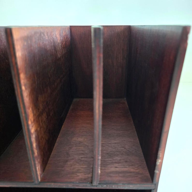 May include: A dark brown wooden desk organizer with three vertical dividers. The organizer has a rectangular shape and is made of stained wood. The dividers create four separate compartments for storing items.