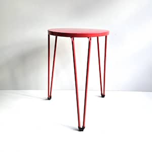 May include: A small, round side table with a vibrant red finish. The table has a circular top and three slender, angled legs. The legs are also red and have black rubber feet. The table is set against a white background.