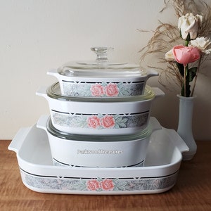 May include: A set of three white casserole dishes with floral designs. The dishes are stacked on top of each other, with the largest dish on the bottom and the smallest dish on top. The dishes have a clear glass lid.