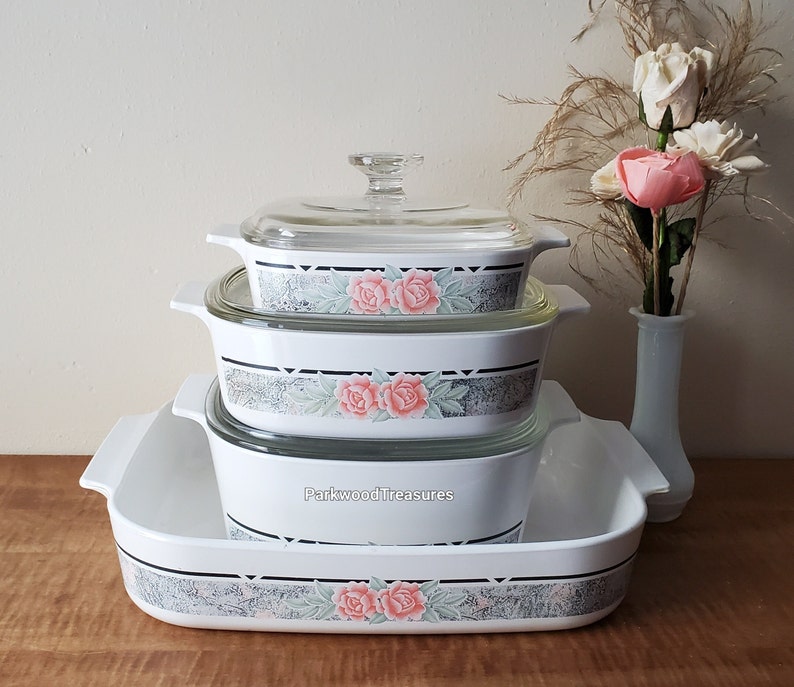 May include: A set of three white casserole dishes with floral designs. The dishes are stacked on top of each other, with the largest dish on the bottom and the smallest dish on top. The dishes have a clear glass lid.