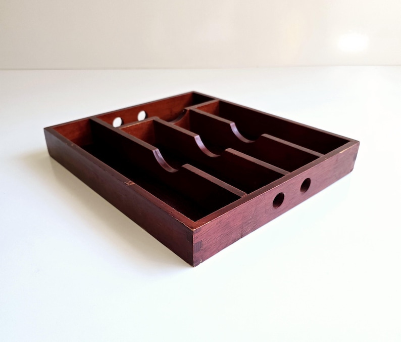 May include: A dark brown wooden cutlery tray with several compartments for organising silverware. The tray has a smooth finish and three small circular holes on one side.