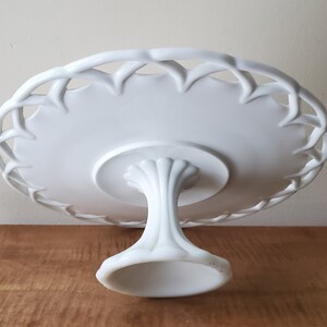 May include: White ceramic cake stand with a delicate, woven-style rim and a pedestal base.