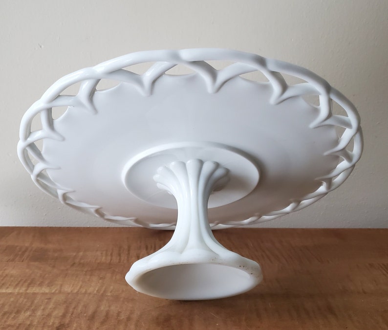 May include: White ceramic cake stand with a delicate, woven-style rim and a pedestal base.