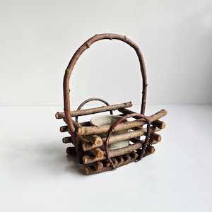 May include: A rustic, handcrafted basket made from natural twigs and branches. The basket features a sturdy handle and a small, light-colored ceramic container inside. The design is simple and organic, perfect for home decor.