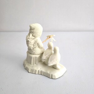 Puede incluir: Figura de cer&aacute;mica blanca que representa un mu&ntilde;eco de nieve con una mochila, sentado en una peque&ntilde;a plataforma con dos focas. El mu&ntilde;eco de nieve sostiene una peque&ntilde;a sombrilla. Coleccionable de invierno.