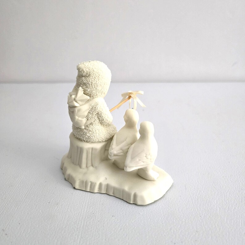 Puede incluir: Figura de cer&aacute;mica blanca que representa un mu&ntilde;eco de nieve con una mochila, sentado en una peque&ntilde;a plataforma con dos focas. El mu&ntilde;eco de nieve sostiene una peque&ntilde;a sombrilla. Coleccionable de invierno.