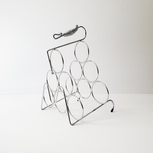 May include: A chrome metal wine rack with a spring-loaded handle. The rack holds 9 bottles of wine.