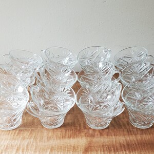 May include: A set of 12 clear glass cups with a starburst pattern. The cups are stacked in two rows of six, with the top row slightly offset from the bottom row.