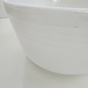 May include: A large, white, circular mixing bowl with a smooth, glossy finish. The exterior of the bowl features a series of subtle, horizontal, raised ridges that wrap around the circumference, providing a textured detail to the simple design.