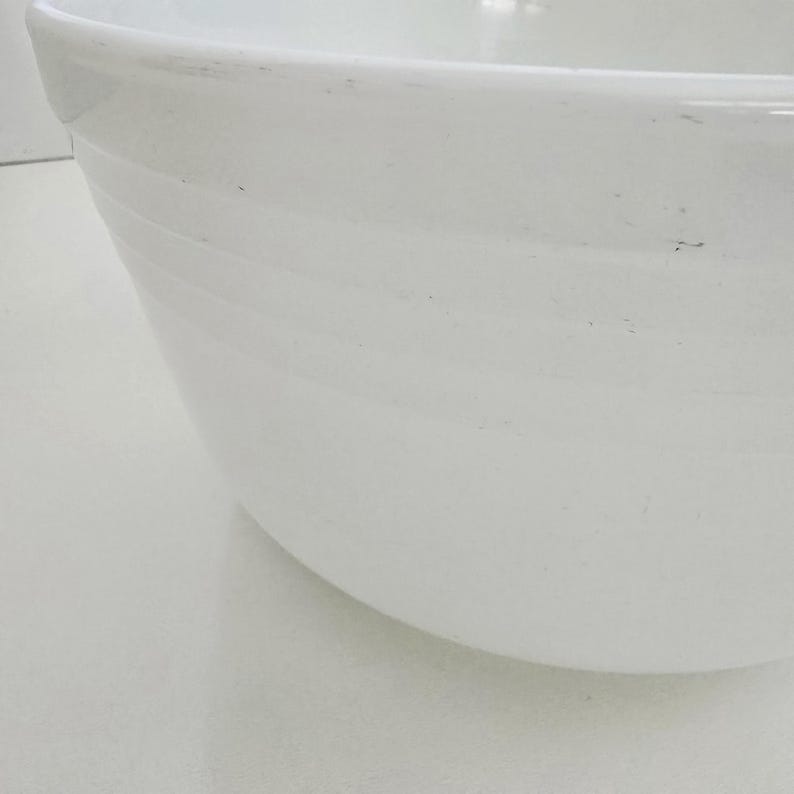 May include: A large, white, circular mixing bowl with a smooth, glossy finish. The exterior of the bowl features a series of subtle, horizontal, raised ridges that wrap around the circumference, providing a textured detail to the simple design.