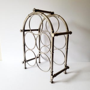 May include: Silver metal wine rack with a curved top and six circular bottle holders.