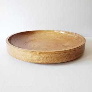 K&ouml;nnte beinhalten: Eine runde Holzschale mit hellbraunem Finish. Die Schale hat einen flachen, gew&ouml;lbten Innenraum und einen dicken, abgerundeten Rand. Die Holzmaserung ist sichtbar und verleiht dem St&uuml;ck Textur. Die Schale wird wahrscheinlich zum Servieren von Speisen oder als Dekorationsartikel verwendet. Durchmesser ca. 30 cm.