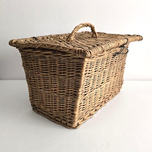May include: A rectangular woven wicker basket with a hinged lid and a handle. The basket is a natural tan color and appears to be handmade. The lid has a curved handle for easy opening and closing.