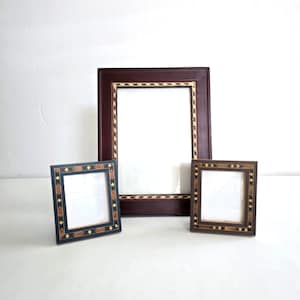 May include: Three decorative picture frames. The largest frame is a deep burgundy with a patterned border. Two smaller frames feature a mosaic-like design in shades of brown and black. All frames have white interiors.