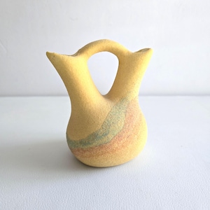 May include: A white ceramic mug with a black handle and the text "But First, Coffee" in a bold, black font. The mug is set against a blurred background, suggesting a cozy setting.