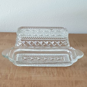 May include: A clear glass butter dish with a decorative diamond pattern. The dish has a lid and a base.