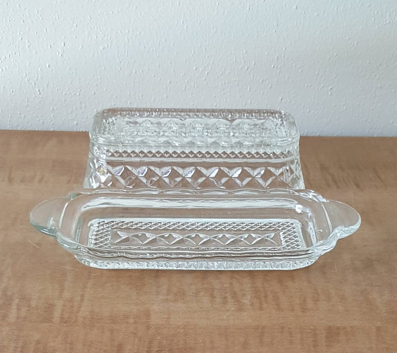 May include: A clear glass butter dish with a decorative diamond pattern. The dish has a lid and a base.