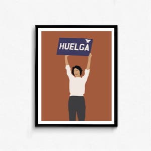May include: A woman holds up a blue sign with the word "HUELGA" in white letters. She is wearing a white shirt and dark pants. The background is a solid orange color.