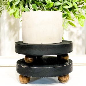 May include: A set of three black wooden tiered risers with a white ceramic planter on top. The risers have a distressed finish and are decorated with wooden ball feet.