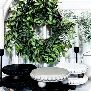 May include: Three tiered wooden display stands with beaded trim. The stands are in black and white with a gray top. The stands are on a white surface with a green wreath in the background.