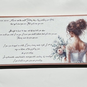 Puede incluir: Una impresión sobre lienzo enmarcada con una ilustración de acuarela de una mujer con un vestido blanco sosteniendo un ramo de flores. El texto en el lienzo dice: "Espejo, espejo. Espejo en la pared Diciendo estas cosas señalando tus defectos Eso no es quien eres. Eso no es quien eres. Puede ser difícil de oír, pero déjame decirte querida Si pudieras ver lo que yo veo, sé que creerías que eso no es quien eres Hay más en quién eres. Te veo vestida de blanco. Todo lo malo se hace bien, veo la furia en flor a la vista de ti. Oh, ve, precioso. Insustituible, inconfundible, incomparable querida, es hermoso Lo veo todo en ti, eres precioso."