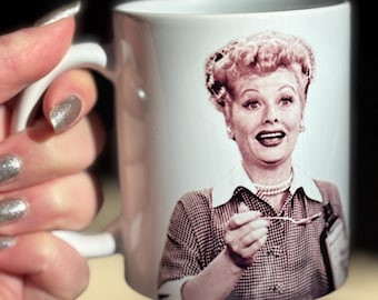 May include: White ceramic mug with a color image of Lucille Ball, a famous actress, printed on the front. She is holding a spoon and looking at the viewer.