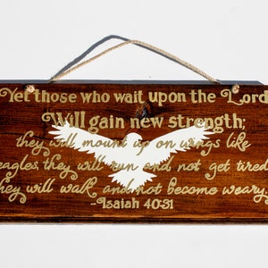 May include: A wooden sign with a white dove silhouette and gold lettering. The sign reads "Yet those who wait upon the Lord Will gain new strength; they will mount up on wings like eagles they will run and not get tired. they will walk and not become weary -Isaiah 40:31"
