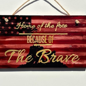 May include: Wooden sign with an American flag design and the text "Home of the free because of the brave".