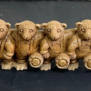 May include: A row of six wooden teddy bears, each wearing overalls and holding a round object. The bears are all facing forward and have a light brown color.