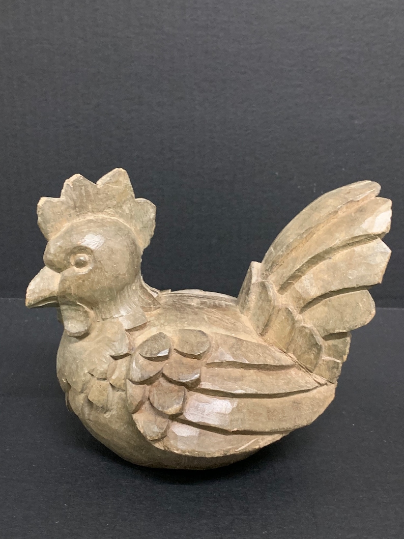 Puede incluir: Una figurita de pollo de madera tallada a mano con plumas detalladas y un pico realista. La figurita est&aacute; pintada en un color marr&oacute;n claro y tiene un aspecto r&uacute;stico.
