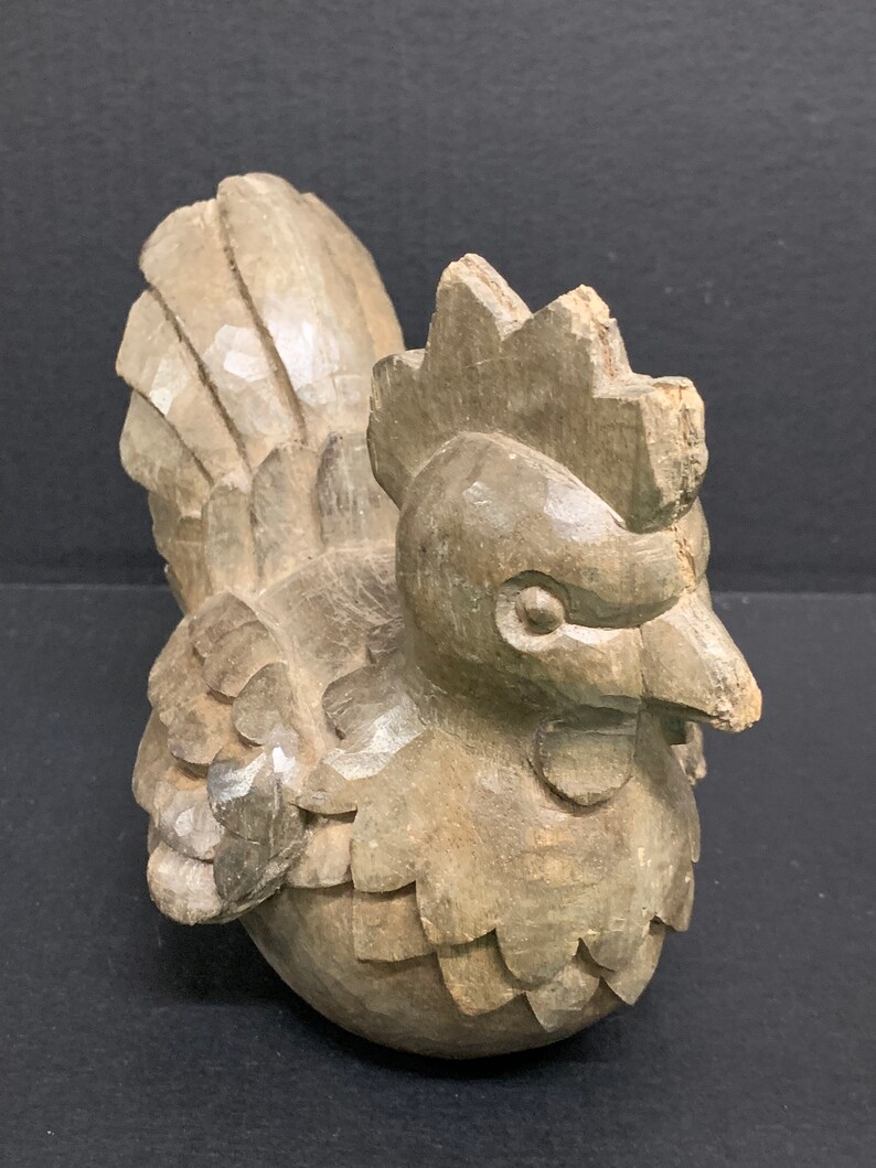 Puede incluir: Una figurita de gallo de madera tallada a mano con un dise&ntilde;o detallado. El gallo es marr&oacute;n y tiene una cresta y un pico prominentes.