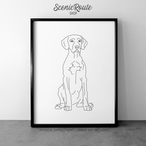 May include: Black framed print featuring a minimalist line drawing of a dog in a seated position. The dog is depicted in black lines against a white background. The text "Scenic Route Shop" is at the top. Below the image is the text "[PHYSICAL SHIPPED PRINT - FRAME NOT INCLUDED]"