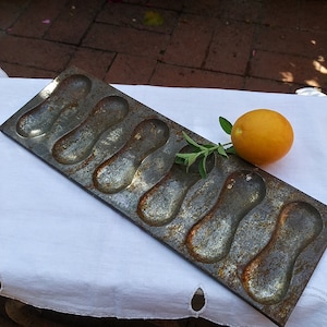 May include: A vintage metal baking pan with eight individual molds shaped like peanut shells. The pan is rusty and has a worn, antique look.