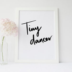 Peut inclure: Impression d'art encadrée blanche avec l'inscription "Tiny dancer" en écriture noire. Un vase en verre transparent avec une fleur rose est à gauche de l'impression.
