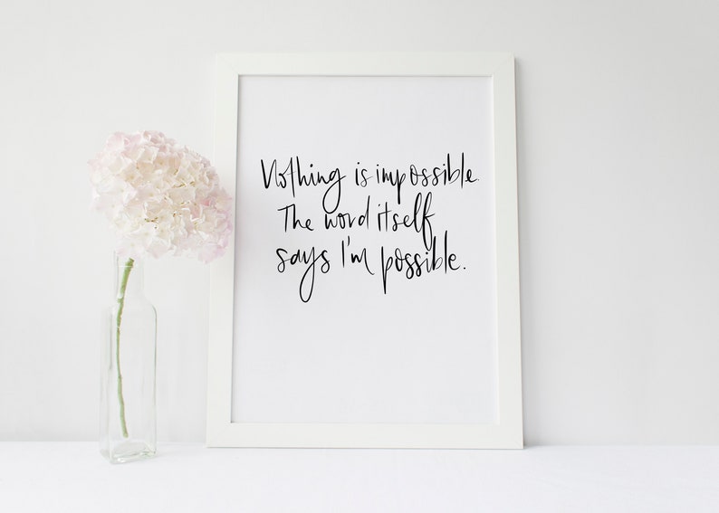 May include: White framed print with the handwritten quote, "Nothing is impossible. The word itself says I'm possible." A clear glass vase holds a pink and white flower arrangement. The background is white.