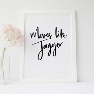 Puede incluir: Impresión enmarcada en blanco con la frase "Moves like Jagger" en escritura negra. A la izquierda, un jarrón de cristal transparente con un arreglo floral rosa. Decoración de pared.